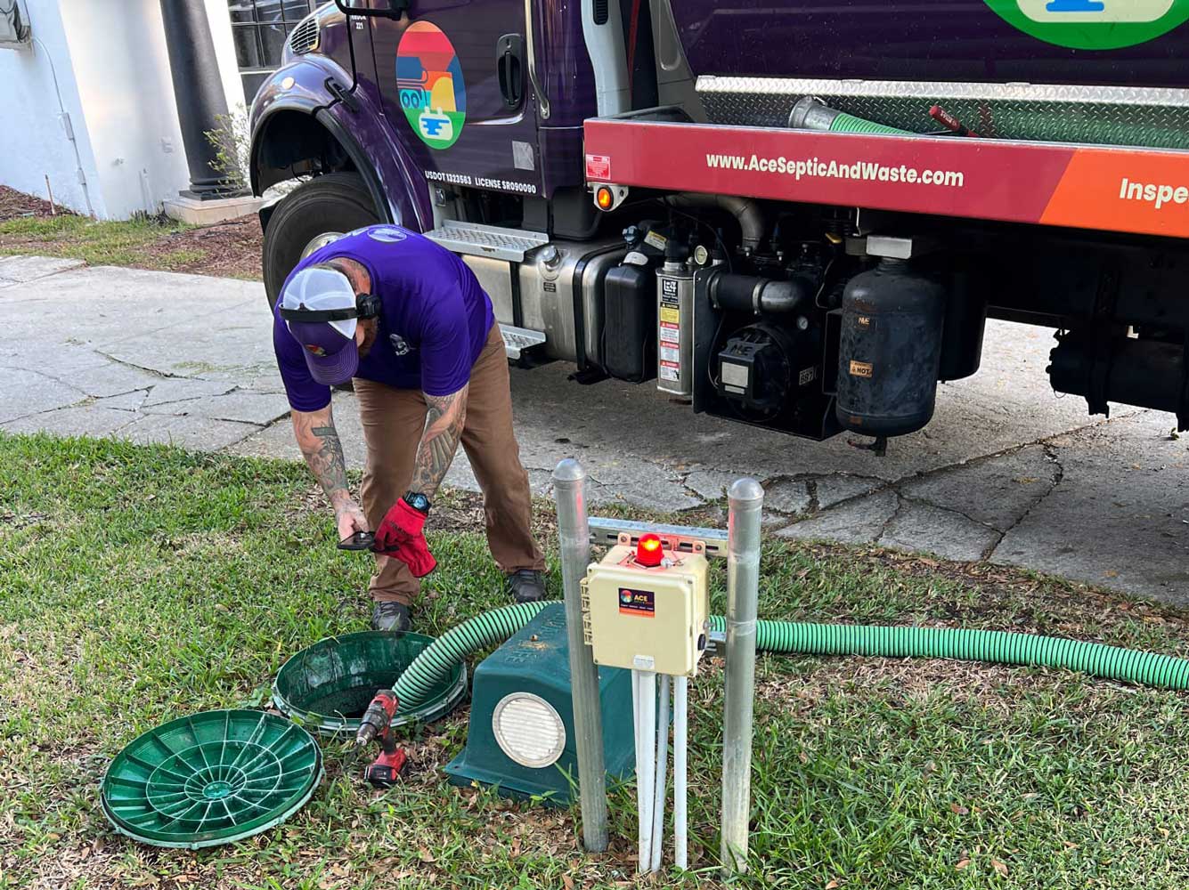 A septic truck with an extended hose across green grass going into a septic system.