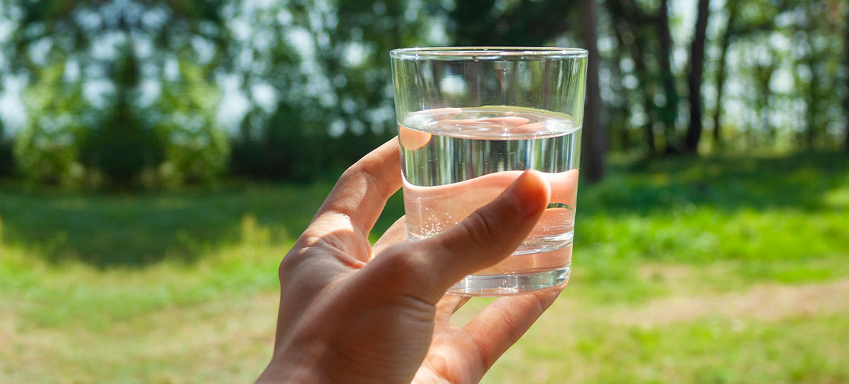 Photo of person holding a glass of water in their backyard