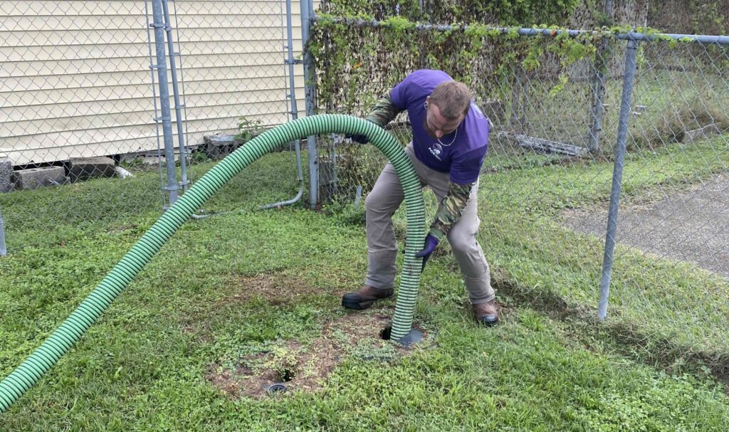 A worker inserting a hose into the ground to pump a septic tank